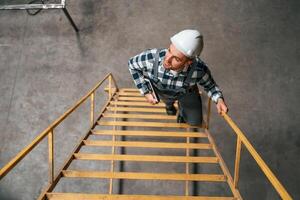 Top view. Going up on the ladder.. Factory male worker in uniform is indoors photo
