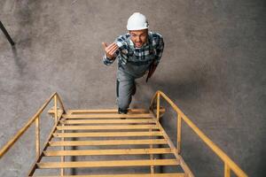 View from the top of ladder. Factory male worker in uniform is indoors photo