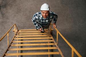 Top ,view. Going up on the ladder. Factory male worker in uniform is indoors photo