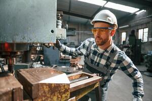 Factory male worker, in uniform is indoors. Operating the drill machine photo