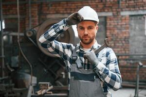 Standing in grey uniform and in ,white hard hat. Factory male worker is indoors photo