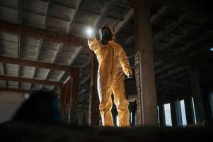 Using the flashlight... Man dressed in chemical protection suit in the ruins of the post apocalyptic building photo