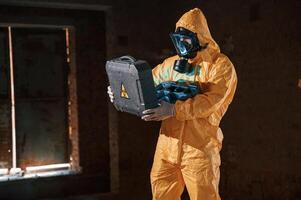 Blue light is, going from hard case that is with hazard sign. Man dressed in chemical protection suit in the ruins of the post apocalyptic building photo