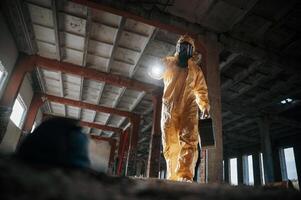 Using the flashlight. Man dressed in chemical, protection. suit in the ruins of the post apocalyptic building photo