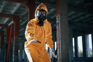 Reaching for an object that is on the ground. Man dressed in chemical protection suit in the ruins of the post apocalyptic building photo