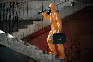 On stairs with flashlight and case. Man dressed in, chemical protection suit in the ruins of the post apocalyptic building photo