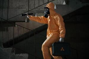 View from the side. Man, dressed, in chemical protection suit in the ruins of the post apocalyptic building photo