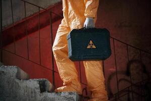 On ,stairs with flashlight and case.. Man dressed in chemical protection suit in the ruins of the post apocalyptic building photo