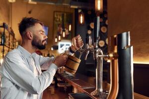 Side ,view. Bartender, pours beer. Man is working in the bar photo