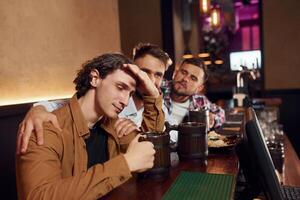 Supporting a sad man. Three friends are in the bar drinking beer and having a good time photo