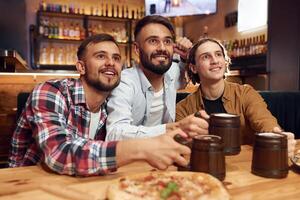 Front view. Soccer fans. Three friends are in the bar drinking beer and having a good time photo