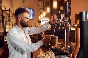 Bartender pours beer. Man is working in the bar. photo