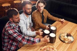 Knocking the mugs. Three friends are in the bar drinking beer and having a good time photo