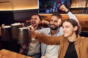 Soccer fans, watching match. Three friends are in the bar drinking beer and having a good time photo