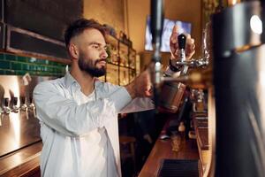 Side view. Bartender, pours beer. Man is working in the bar photo