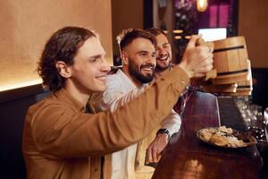 Raising up the mugs.. Three friends are in the bar drinking beer and having a good time photo