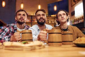 Watching TV. Three, friends are in the bar drinking beer and having a good time photo