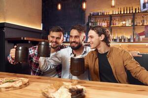 Knocking the, mugs. Three friends are in the bar drinking beer and having a good time photo