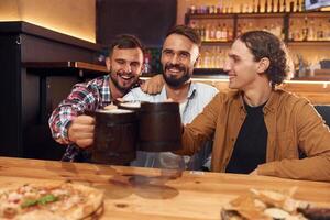 Raising, up the mugs. Three friends are in the bar drinking beer and having a good time photo