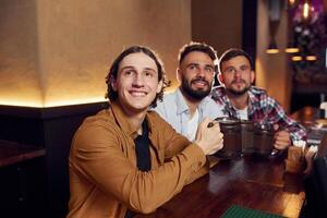 Sitting, and smiling. Three friends are, in the bar drinking beer and having a good time photo