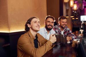 Sitting, and smiling. Three friends are in the, bar drinking beer and having a good time photo