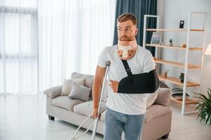 Front view. Man with crutches ,is walking at home indoors. Having injuries photo