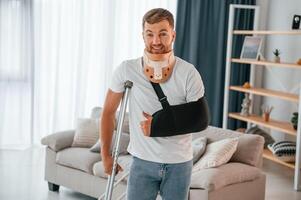 Front view. Man with crutches is walking at home, indoors. Having injuries photo
