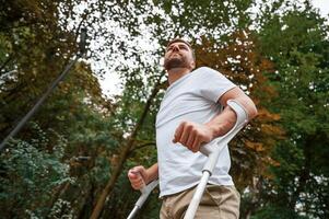 Walking,, view from below. Man with crutches is in the park outdoors. Having leg injury photo