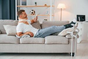 Laying down and ,resting on the sofa. Man with crutches is at home indoors. Having injuries photo