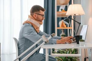 Working ,from home ,by using laptop. Man with crutches is indoors. Having injuries photo