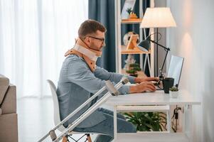 Working from home by ,using laptop. Man with crutches is indoors. Having injuries photo