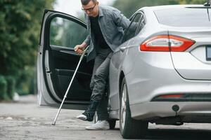 Injured man with crutches is going out from the car.,. photo