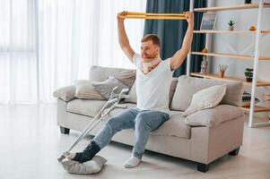 Rehabilitation exercises, for, arms. Man with crutches is at home indoors. Having injuries photo