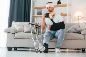 Drinking from the cup. Man with ,crutches is at home indoors. Having injuries photo