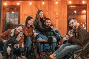 Coneption ,of weekend. Group of people is together near beautiful wooden building at evening time photo