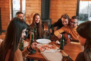 With pizza and, beer. Group of friends is having good weekend indoors in the wooden building together photo