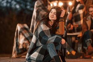 Portrait, is sitting in front of her friends. Group of people is spending time together on the backyard at evening time photo