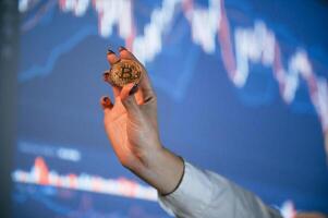 Close ,up view of woman's hand that holding physical bitcoin against background with graphs photo