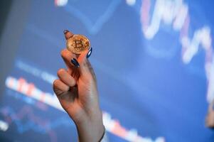Close up ,view of woman's hand that holding physical bitcoin against background with graphs photo