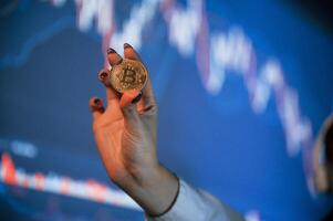 Close up view of woman's hand that holding ,physical bitcoin against background with graphs photo