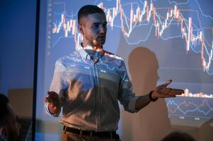 Man i,s standing near projector and showing graphs and business graphs photo