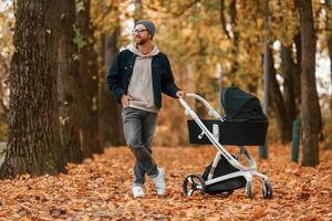 Standing and enjoying a nature. Man ,with pram is having a walk in the autumn park photo