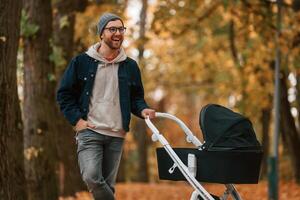 Front view.. Man with pram is having, a walk in the autumn park photo