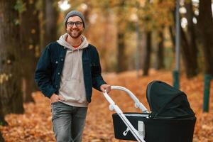 Front view. Man with pram is having a walk in the ,autumn park photo