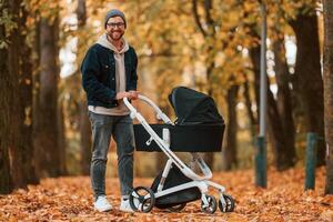 Standing and enjoying a nature. Man with pram, is having a walk in the autumn park photo