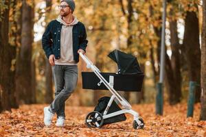 Standing ,and enjoying a nature.. Man with pram ,is having a walk in the autumn park photo