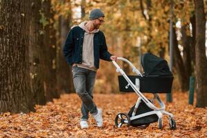 Standing and enjoying a nature.. Man with ,pram is having a walk in the autumn park photo