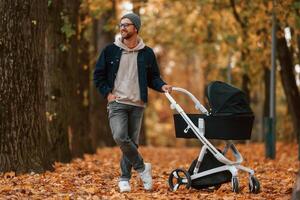 Front view. Man with pram is having a walk in the autumn park, photo