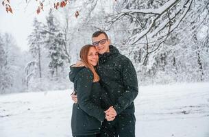 Standing and posing while embracing ,each other. Couple is in the winter forest, having a walk photo