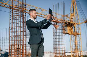 Holding tablet. Businessman in formal clothes is on the construction site at daytime photo
